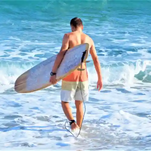 Man wearing grition sandals at the beach and holding a surfboard 